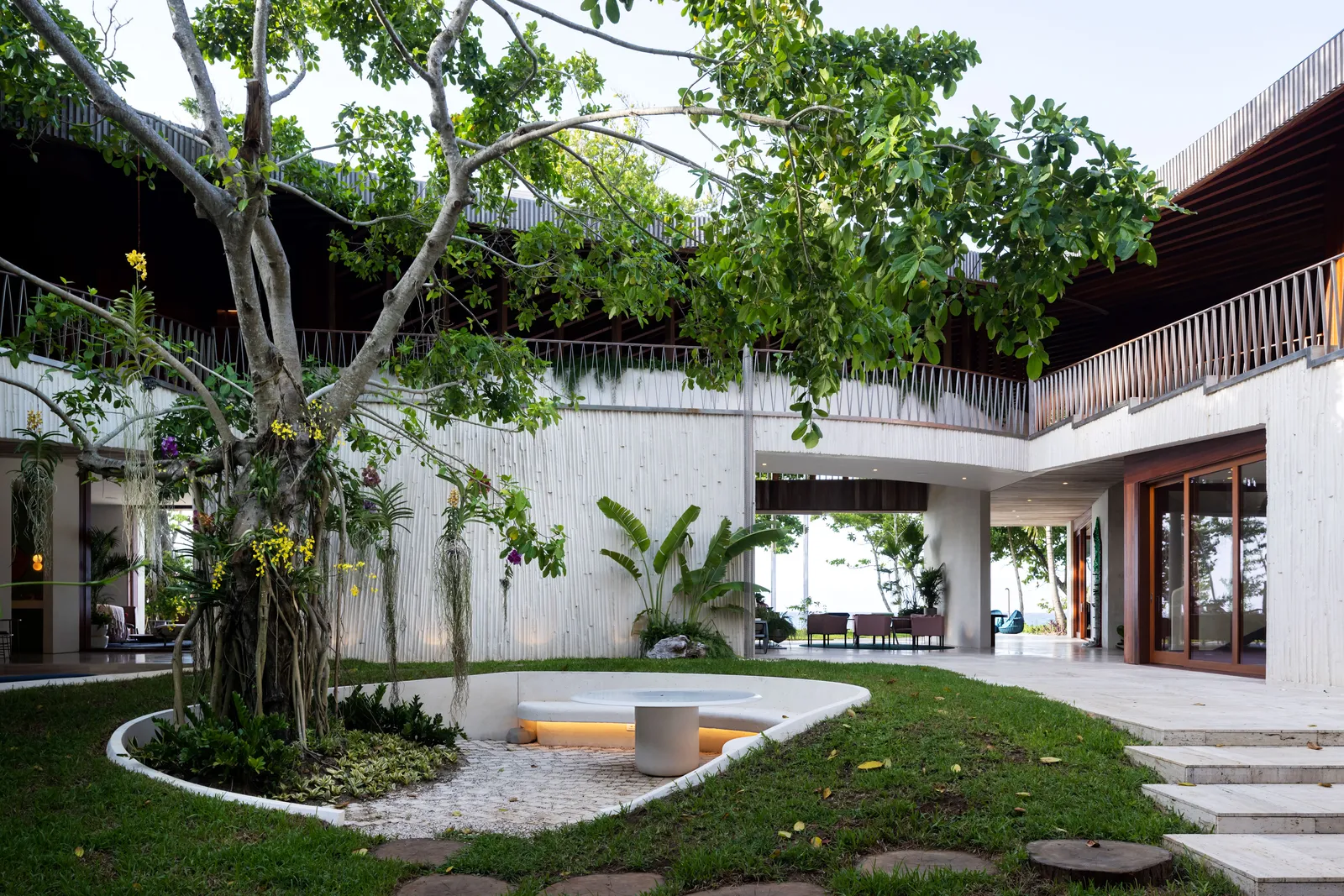 Playa Grande II — central courtyard tree, perforated white facade, and the Atlantic horizon beyond